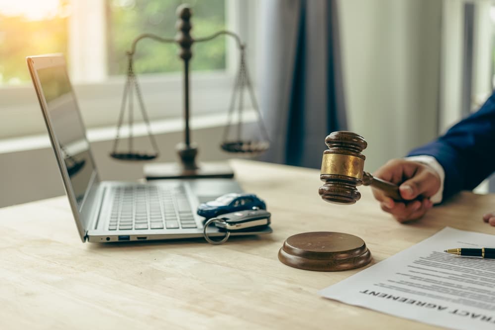 Lawyer, judge's gavel and miniature car as symbols of auction or court action against driver who got into an accident and received car insurance money on the table.