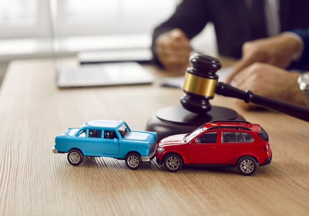 Little crashed autos on table in courtroom. Gavel and two small toy car models on desk in courthouse. Concept of lawyer services.